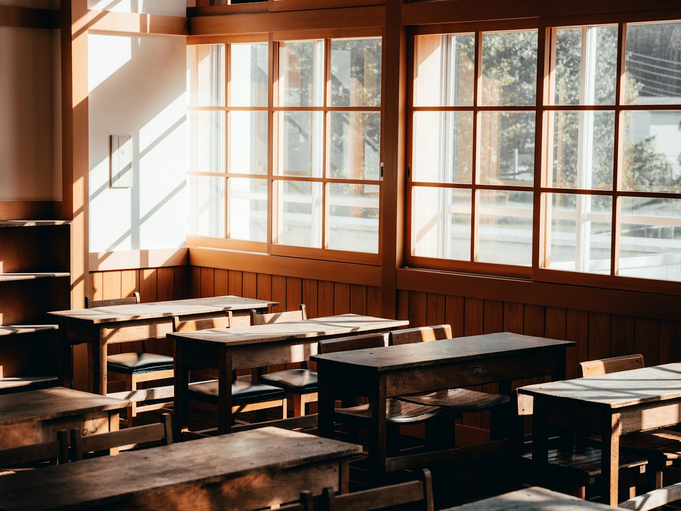 An empty vintage classroom with wooden desks and tall windows full of warm sunlight