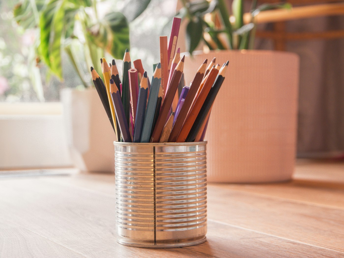 Sharpened pencils in a tin can on a wooden desk in soft window light
